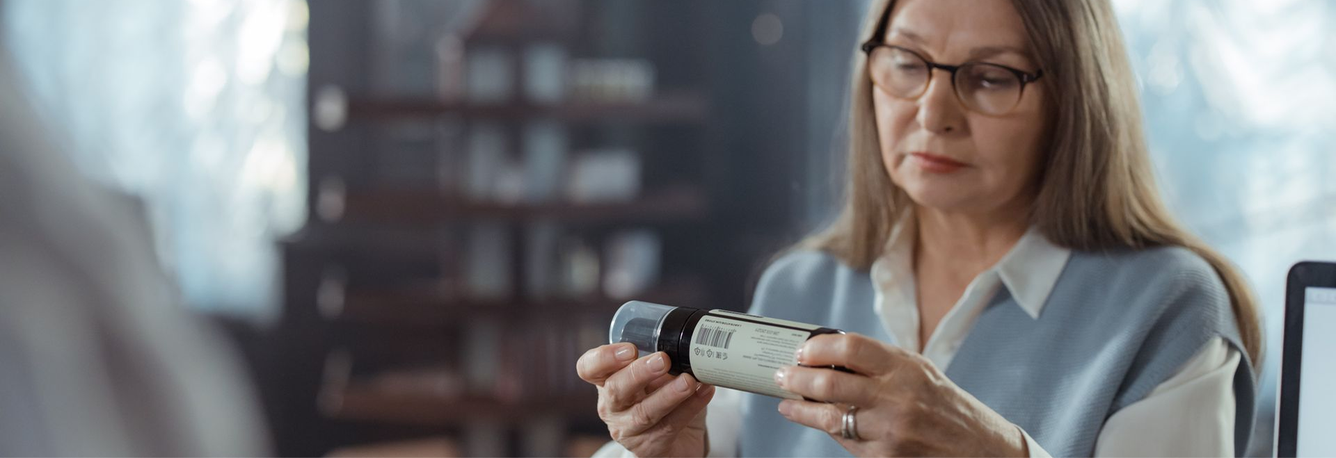 A senior woman with eyeglasses reviewing a medicine bottle at a pharmacy counter